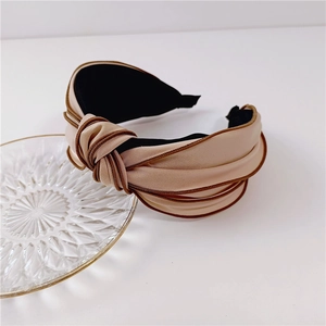 Close-up of beige wide-brimmed knotted headband with elegant brown trim and black lining
