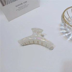 Detail showing pearlescent acetate hair claw clip with iridescent finish on white desk