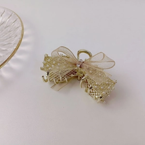 Détail de pince à cheveux dorée avec nœud en organza, perles et strass brillants