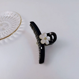 Gros plan détaillé d'une pince à cheveux noire avec fleur blanche et détails dorés