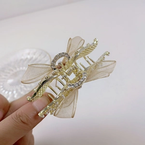 Détail de la pince à cheveux dorée avec perles, strass et nœud en organza champagne en main