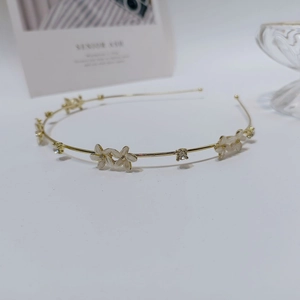 Detailed macro view of thin golden metal headband with white floral resin charms and rhinestones