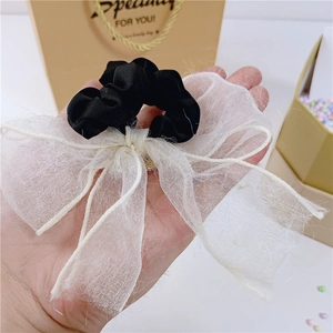 Détail d'un chouchou à nœud en dentelle noir et blanc tenu à la main avec boîte cadeau