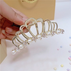 Dettaglio di un fermaglio per capelli in metallo dorato con perle bianche e strass lucidi