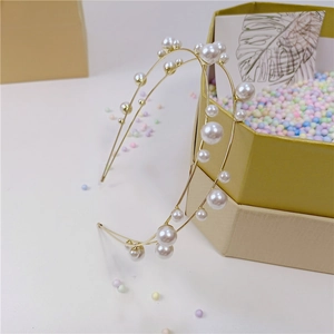 Dettaglio del cerchietto doppio in metallo dorato con perle su una confezione regalo elegante
