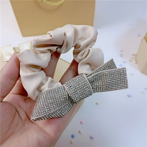 Close-up of cream satin scrunchie featuring a luxury rhinestone bow detail