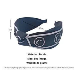 Détail d'un serre-tête large bleu marine avec broderie smiley et bordure blanche