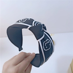 Gros plan d'un serre-tête noué en tissu noir avec motifs de smileys blancs tissés