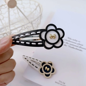 Detail of floral hair clip featuring leather edges and a golden bow on black fabric