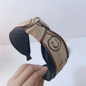 Vue détaillée du serre-tête tricoté beige orné de motifs souriants de couleur marron