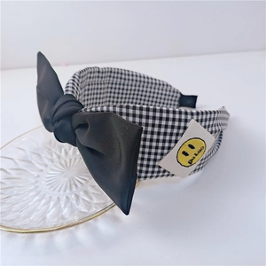 Détail du serre-tête en tissu à carreaux avec grand nœud noir et étiquette smiley
