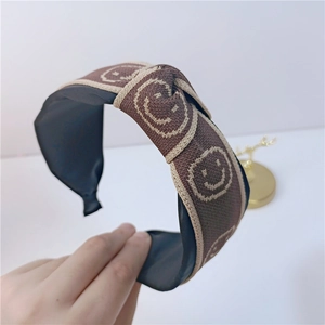 Gros plan sur un bandeau en tricot marron avec motif smiley beige et détail de nœud
