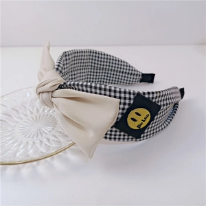 Détail du serre-tête en tissu à carreaux avec un patch smiley jaune et nœud beige
