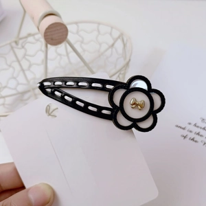 Elegant black and white camellia flower hair clip with a golden bow and leather edge detail
