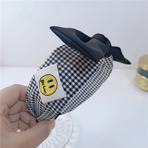 Détail du serre-tête en tissu à carreaux avec un grand nœud noir et un écusson souriant