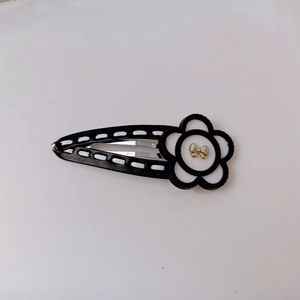 Detailed close-up of a black and white floral hair clip with a golden bow accent
