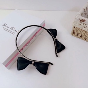 Detail of elegant black satin bow headband with sparkling white rhinestones on white desk