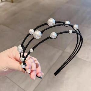 Detail view of a triple-layered black headband with elegant white faux pearls