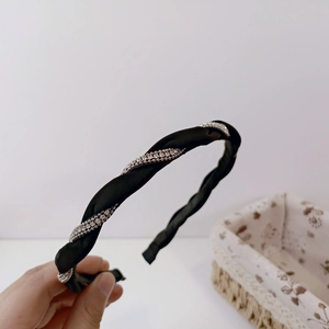 Detail of a black braided headband with satin texture and spiral rhinestone embellishments