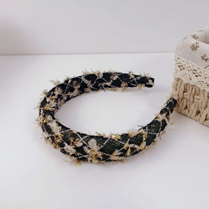 Detail of tweed headband with dark green and white plaid pattern and gold fringe texture