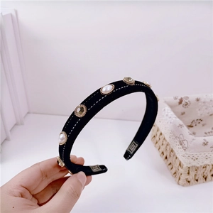 Detailed macro view of black velvet headband with pearls, rhinestones, and white stitching