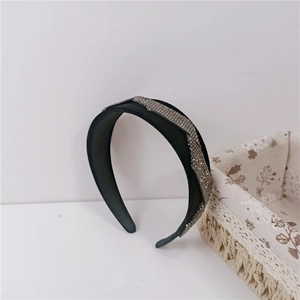 Close-up of black velvet headband with dense grey rhinestone wrap detailing on white surface