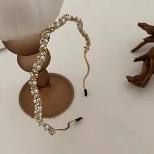 Detail of elegant gold wavy headband featuring white pearls and beads on vintage stand