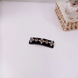 Close-up of a black rectangular hair clip with white pearl flowers and gold gems