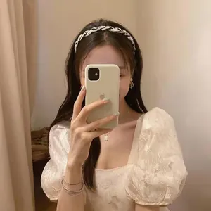 Detail view of woven white headband with pearl accents worn by a model in a mirror selfie