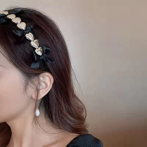 Détail d'un serre-tête en satin noir avec coeurs métalliques et nœuds sur modèle