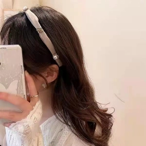 Detail of grey mesh headband with pearls, butterfly earrings and a gold ring on a model