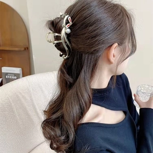 Détail d'une pince à cheveux en métal doré avec perle et accents rouges sur les cheveux