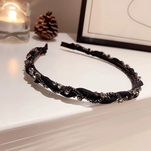 Dettaglio di un cerchietto in tessuto nero con strass e catena metallica intrecciata