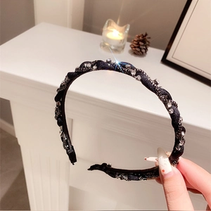 Dettaglio del cerchietto a treccia nera con strass scintillanti tenuto in mano in interni