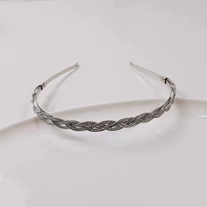 Macro detail of a silver braided metal headband on a minimalist white ceramic plate