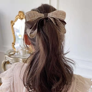 Brown bow hair clip with tweed pattern detail shown on model's ponytail hairstyle