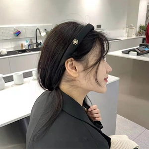 Détail d'un serre-tête rembourré en tissu noir avec breloque fleur dorée sur modèle