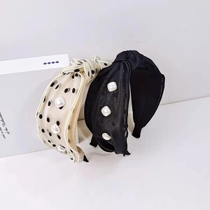 Detail of wide-brimmed knotted headbands with pearl accents in beige polka dot and black fabric