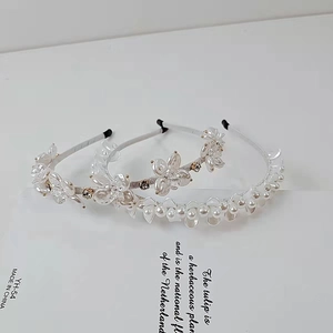 Dettaglio di tre cerchietti con fiori in perle e cristallo su un supporto bianco minimale