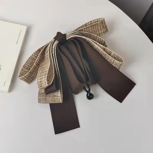 Detail of tweed and dark brown satin bow banana clip hair accessory on a white table