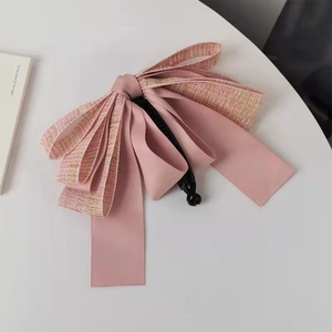 Close-up of pink tweed and ribbon bow banana hair clip on a minimalist white desk