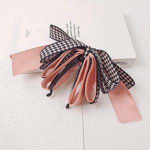 Barrette banane à nœud en satin rose et pied-de-poule sur un livre blanc décoratif