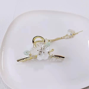 Dettaglio di un fermaglio per capelli a fiori dorati con petali bianchi e nappe di perle