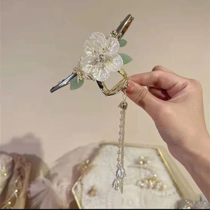 Dettaglio del fermaglio per capelli dorato con fiori bianchi e lunghi pendenti a nappa