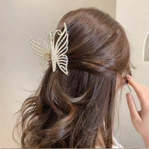 Detail of golden butterfly hair claw with white pearls on a model's hair