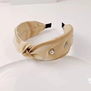 Details des beigen Falten-Haarreifens mit eleganter Perle und Strass-Herz-Anhänger