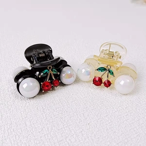 Detail view of pearl hair clips with red rhinestone cherry charms in black and amber colors