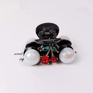 Detail of a black hair claw clip featuring pearl embellishments and a red crystal cherry