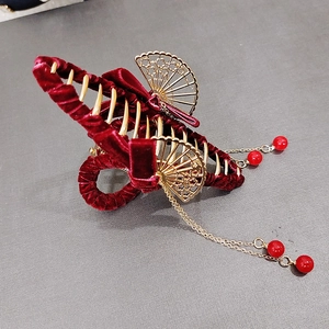 Dettaglio di un fermaglio per capelli in velluto rosso con ventaglio dorato e nappe