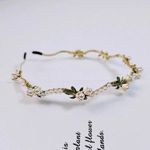 Detailed shot of golden lily of the valley headband with white pearls and green leaves